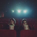 Melhores filmes de terror de 2026 até agora - Duas pessoas assistem assustadas a um filme enquanto comem pipoca em uma grande sala de cinema quase vazia