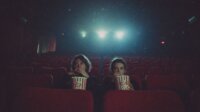 Melhores filmes de terror de 2026 até agora - Duas pessoas assistem assustadas a um filme enquanto comem pipoca em uma grande sala de cinema quase vazia